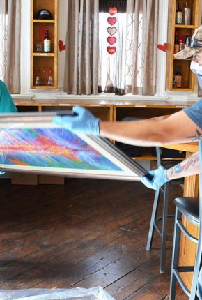 ABOVE: Workers prepare Arthur Miller’s artwork for shipment to a U.S. Embassy in Africa. RIGHT: Miller shows one of his works selected for display in the official residence of Sandra E. Clark, the U.S. ambassador to Burkina Fasou in West Africa.