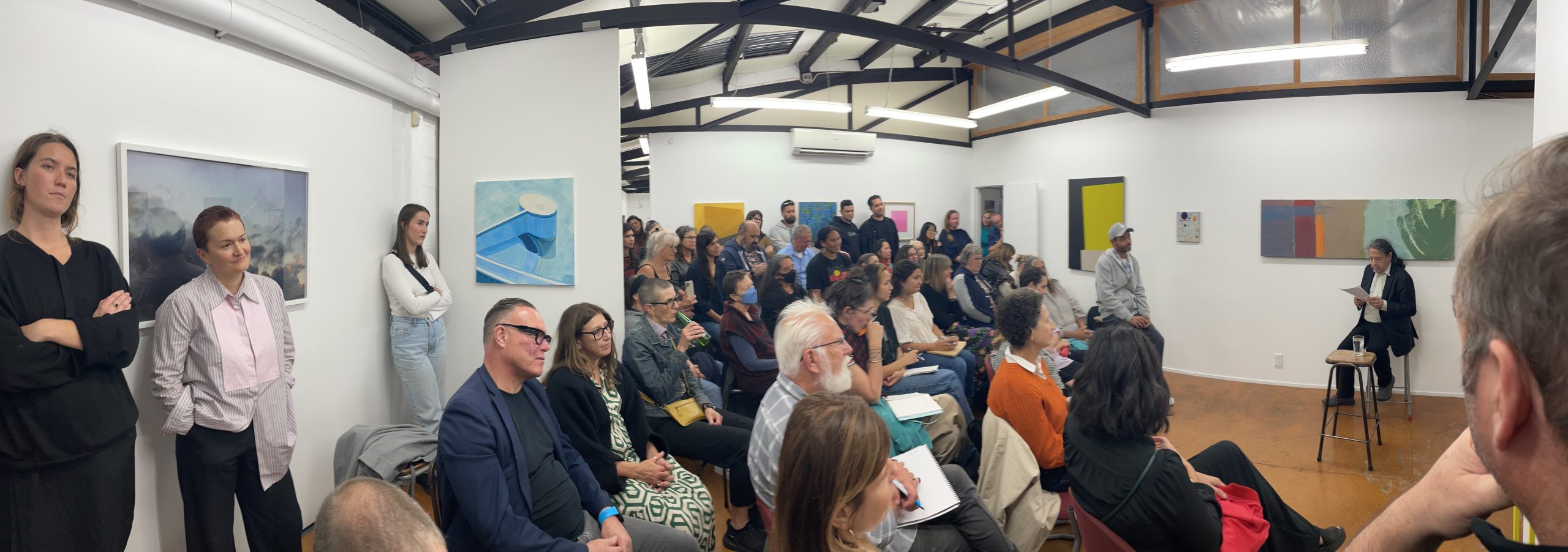 Smith speaks to a large assembled group in a gallery about his experiences as an activist, critic, and curator making sense of the contemporary landscape of Indigenous art in the United States and the way it echoes and differs from the work of artists in Aotearoa, or New Zealand.