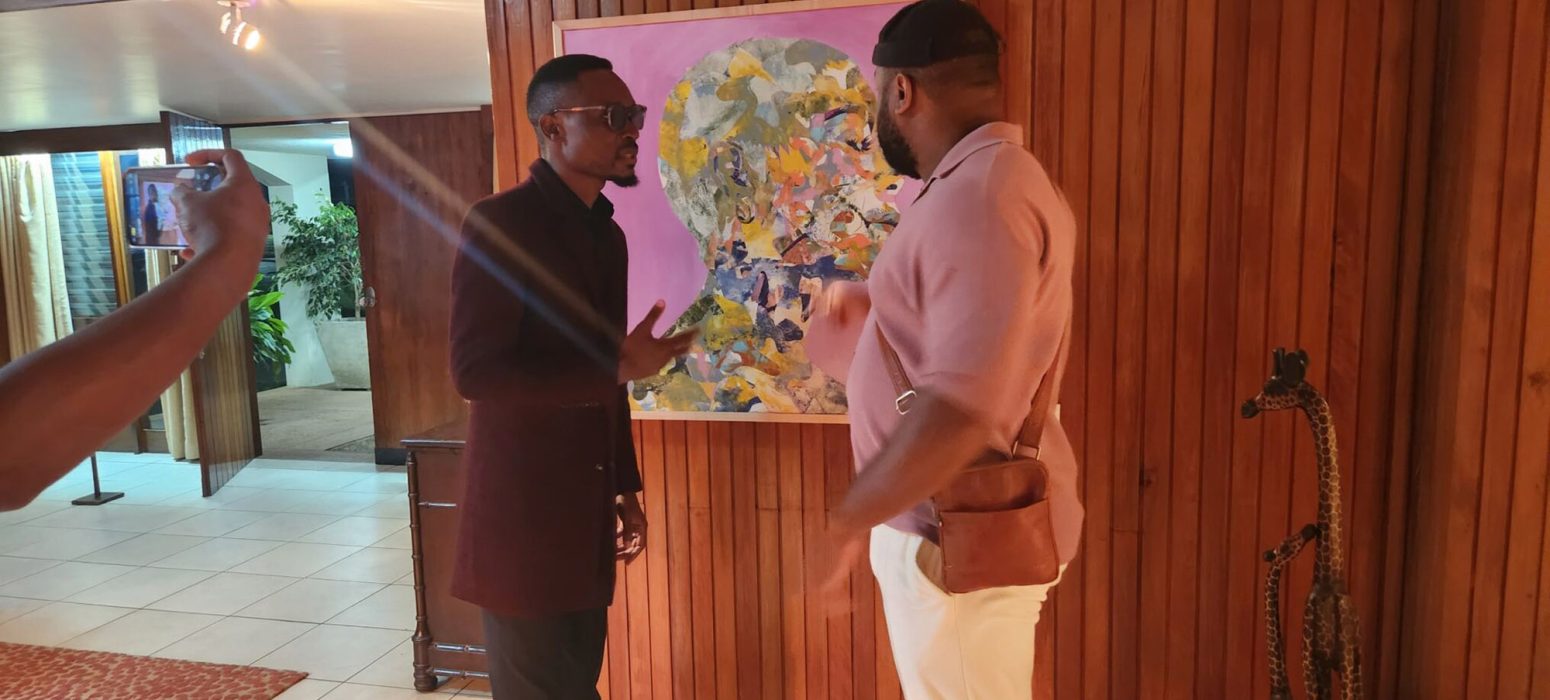 Jean-Pierre speaks with a Malawian artist at a reception at the Residence of U.S. Ambassador David Young, standing in front of his painting Autobiography of My Mother II.